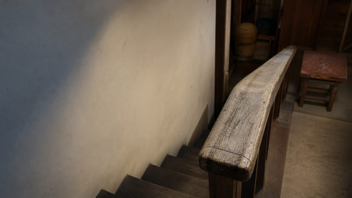A worn wooden handrail running down a staircase, its finish rubbed smooth where hands have gripped it.